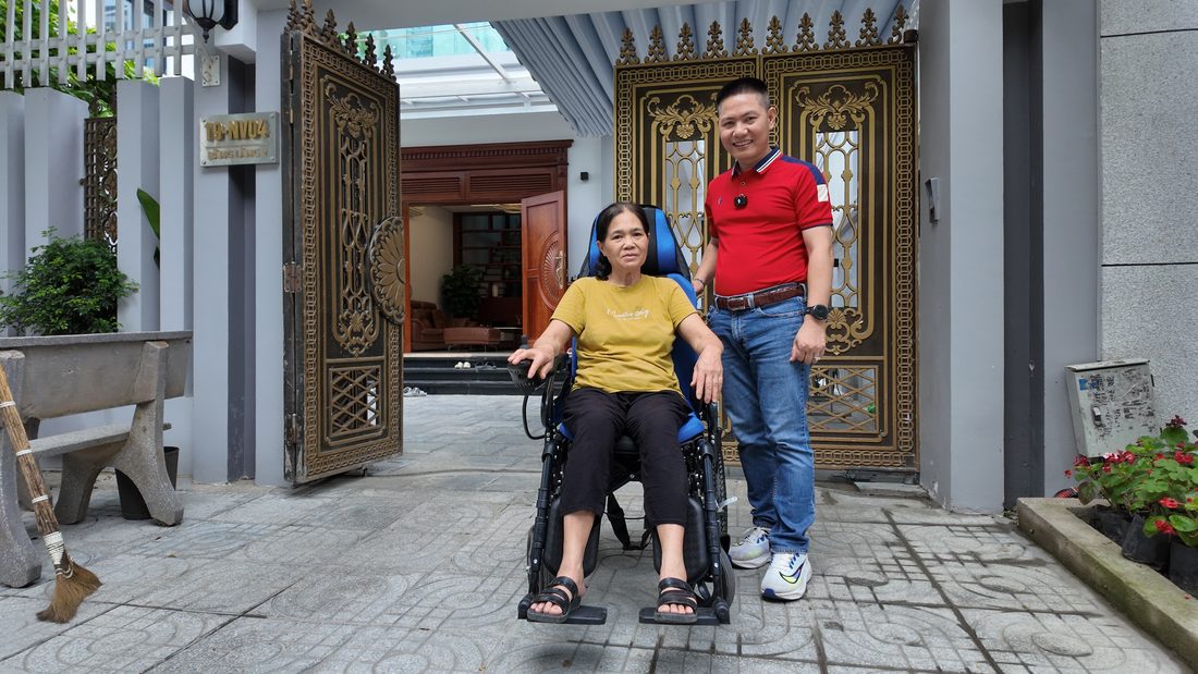 Khách hàng lớn tuổi ngồi trên xe lăn điện mới trước cổng nhà, nhân viên 3T Mart đứng cạnh